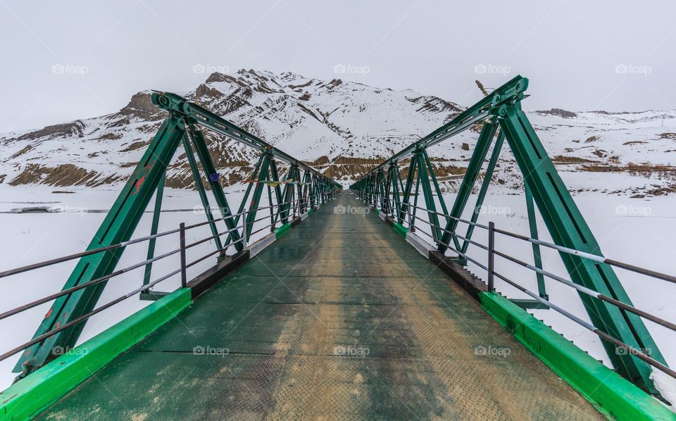 wooden bridge surrounded by snow capped mountains