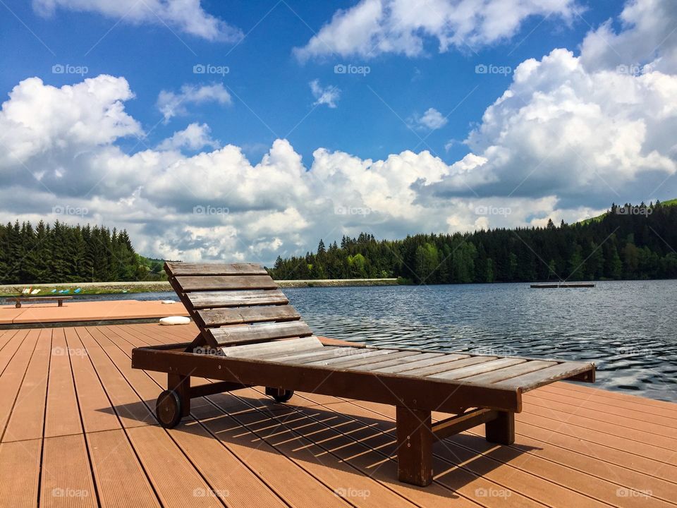 Empty wooden sunbed near the lake on a day with sun and clouds