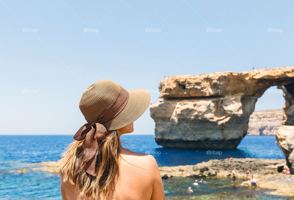 Rear view of woman with hat standing near the sea