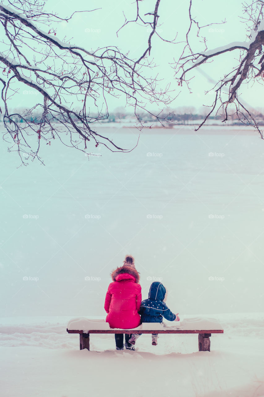 Mother and her little daughter are spending time together walking outdoors in forest in winter while snow falling going through deep snow enjoying wintertime