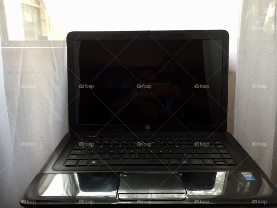 A black laptop computer in front of a window with white sheer curtains
