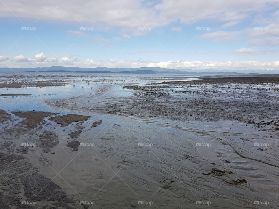 Parksville Beach, sand and sea water when tide is out, with blue sky with clouds on summer day