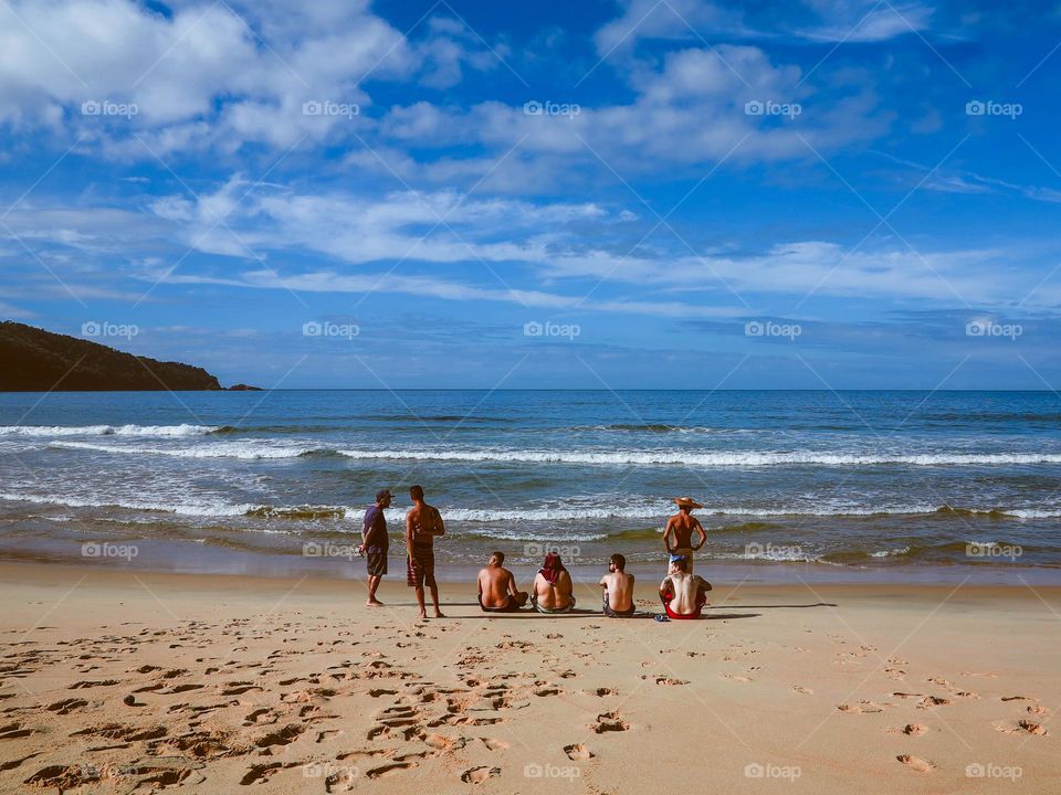 Beautiful shot of the Sunrise on the Atlantic ocean, in Praia do Sono, Brasil. There are 7 men sitting on the beach sand, with a beautiful blue sky ahead.