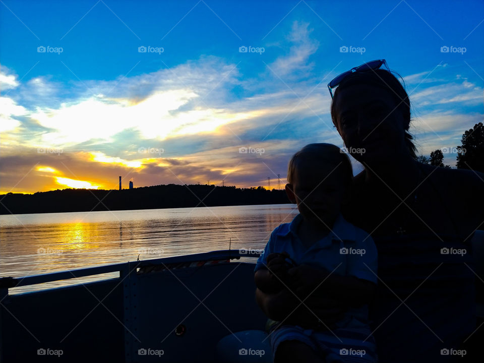 Mother and Son silhouetted on a boat with lake and gorgeous sunset in back. Duke Power Steam station