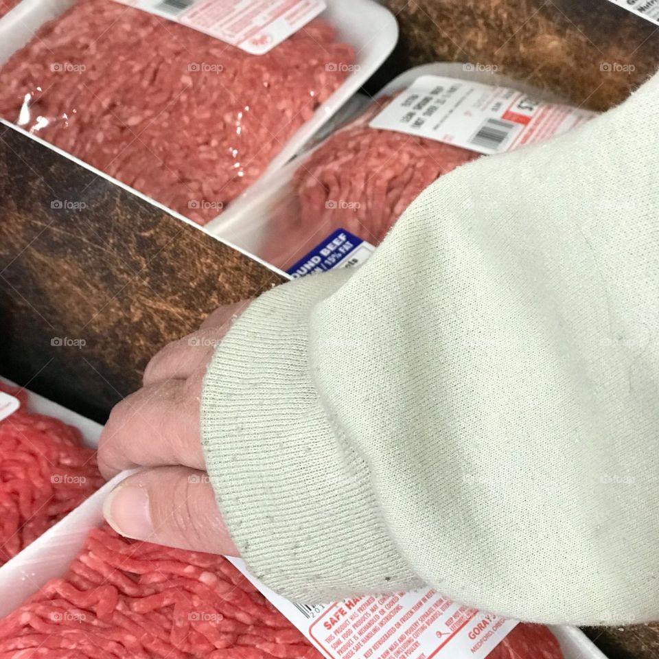 A woman chooses a package of hamburger from the meat section of the local supermarket. 