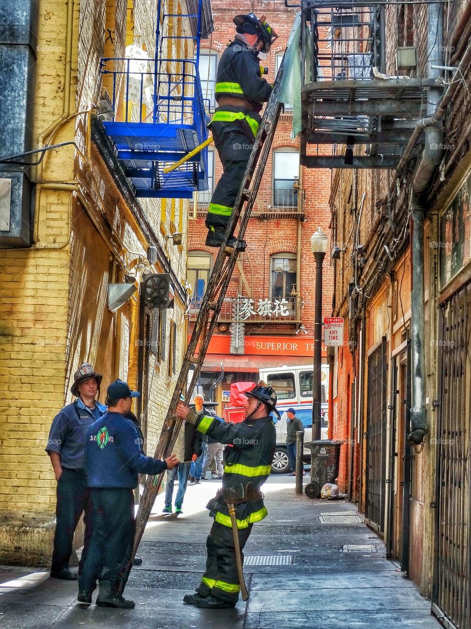 Firefighters In A City Alley. Firemen Scaling A Ladder Into A Highrise Apartment Building
