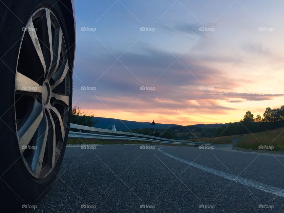 Focus on car wheel on the road with sunset ahead