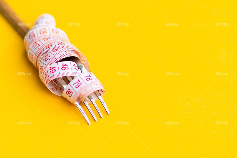 Fork and measuring tape on yellow background 