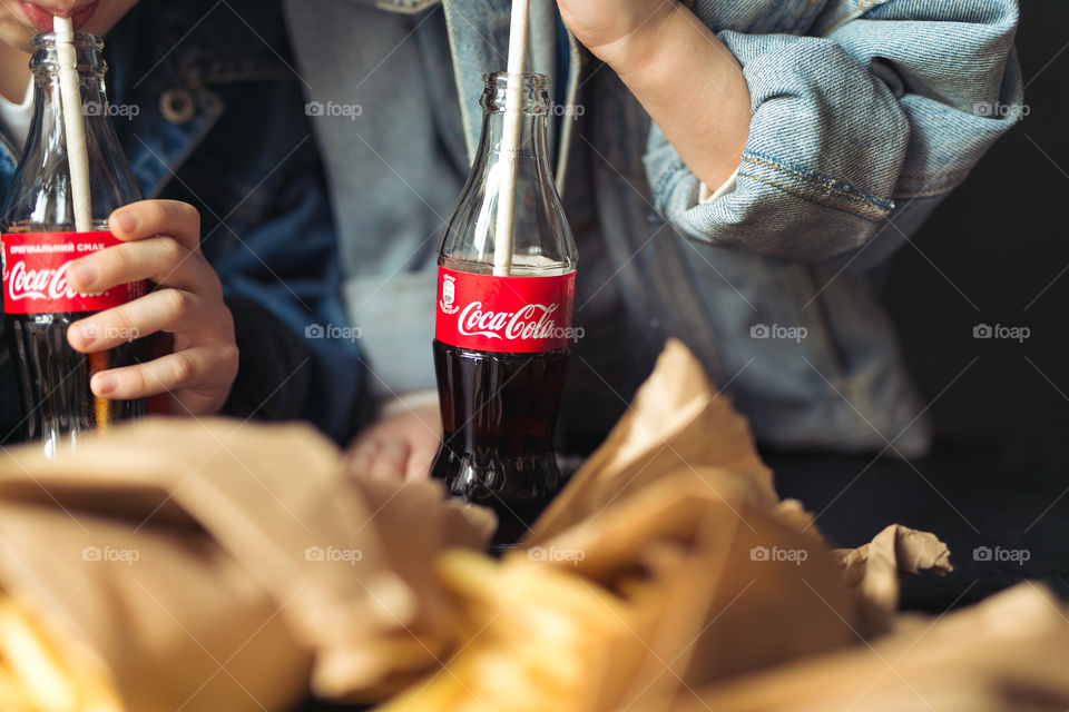 cute guys, brother and sister, move out, rejoice, spend time together and drink Coca-Cola. children are dressed in denim clothes, black background. bottles with coca-cola glass