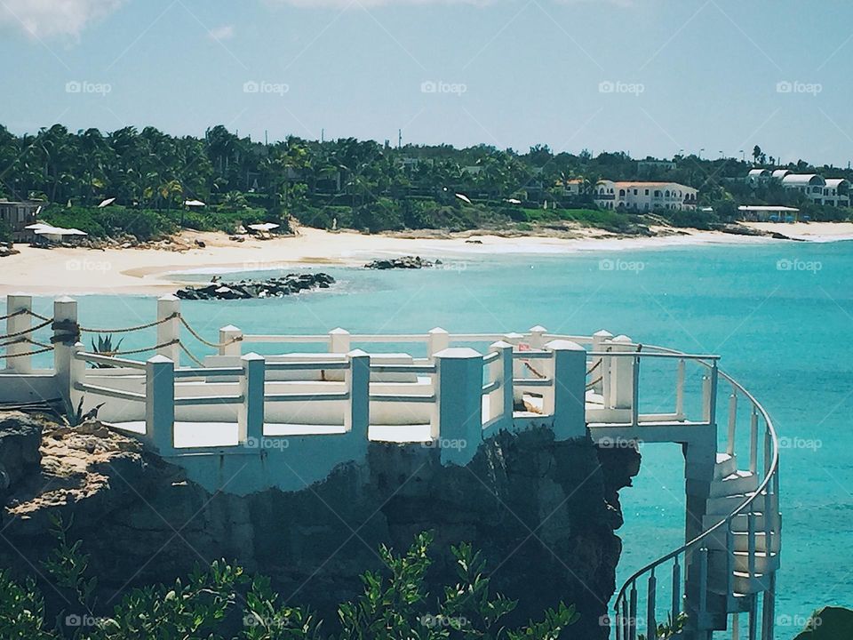 Beautiful sight overlooking the ocean with a walk-way on a cliff leading down a spiral staircase and into the water. 
