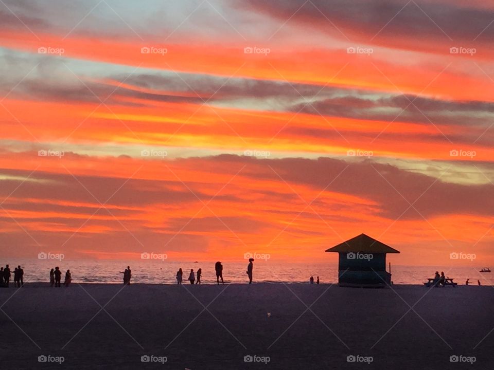 Sunset at the beach with vivid colors of orange and silhouettes of people and a bath house 