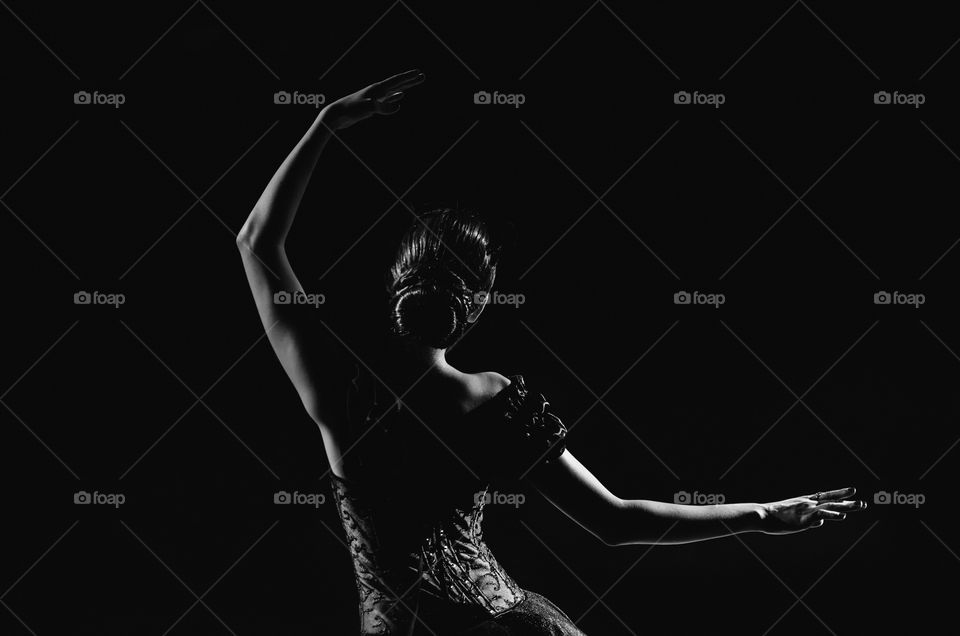 Light silhouette of elegant young ballerina standing back to camera in third position arms petite pose on the background