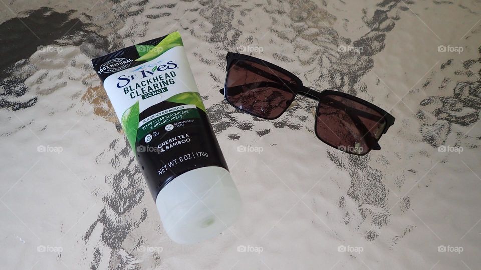 Beauty products I love St. Ives exfoliant cream bottle sunglasses on frosted glass background 