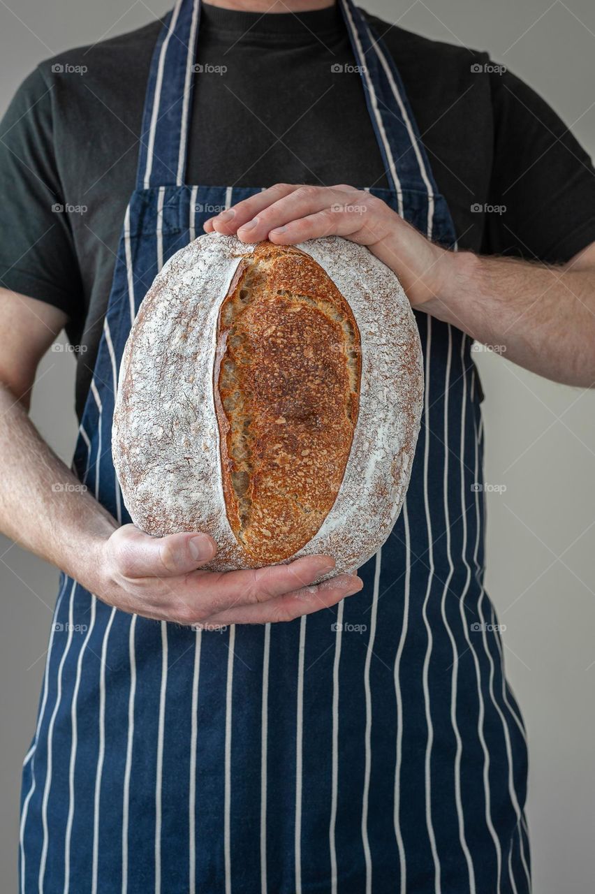 Close-up at bakers hands holding a loaf of sourdough bread in front of him.