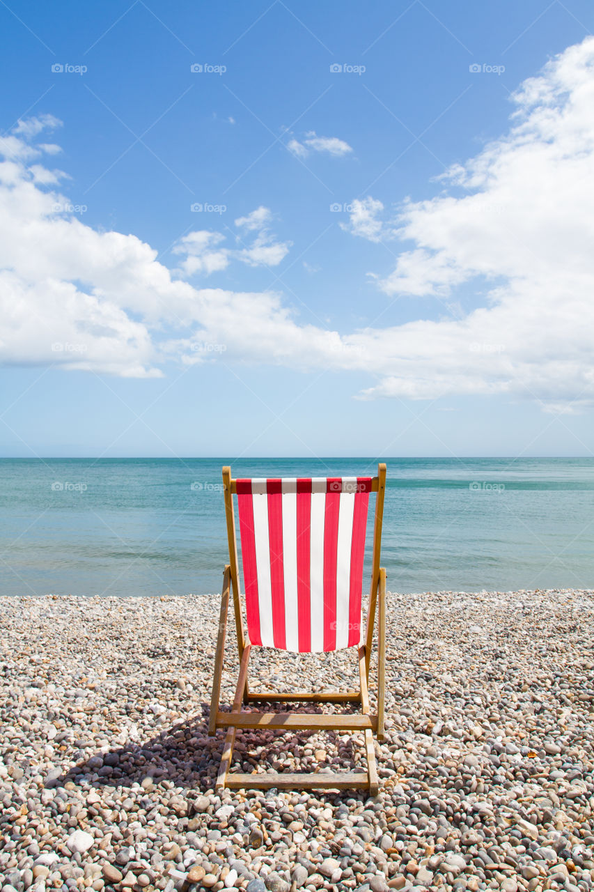 Red Striped Deckchair. A single red and white striped deckchair on a pebble beach