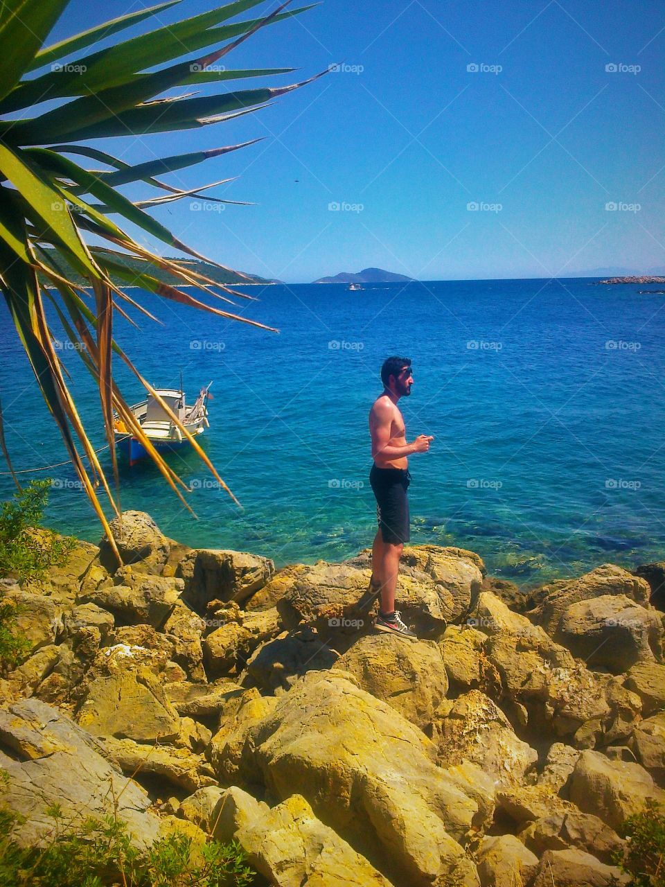 Shirtless man standing on rock near the sea