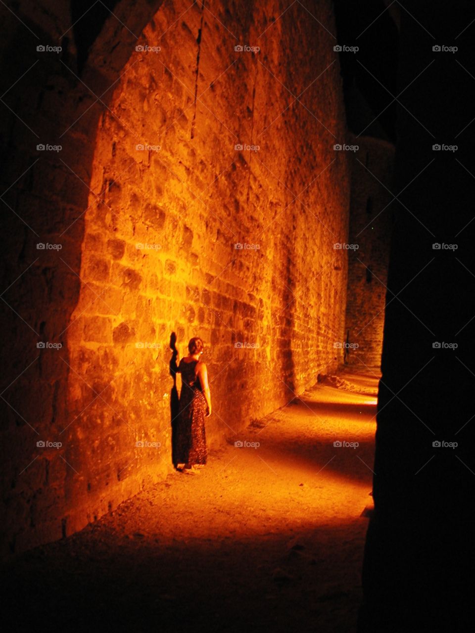 A lonely night in Carcassonne. Alone woman in a dress stands beside the entrance wall of the castle in Carcassonne