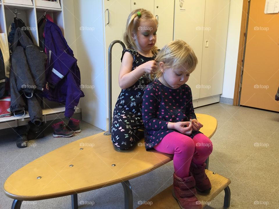 Big sister is helping little sister with her hair at their kindergarden school.