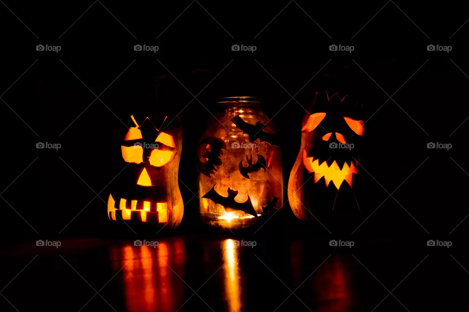 Two evil pumpkins and a jar of bats in a dark room on Halloween.