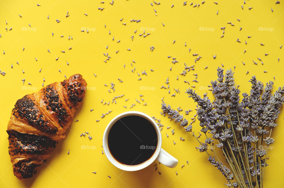 Business working morning with cup of hot coffee, sweet croissant, lavender flowers on yellow background close up. Top view, copy space, flat lay, mockup.