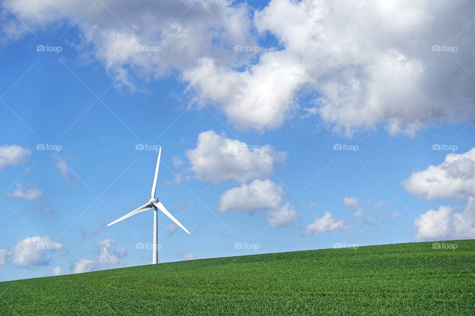 One wind turbine on a green hill with blue sky and white clouds in background