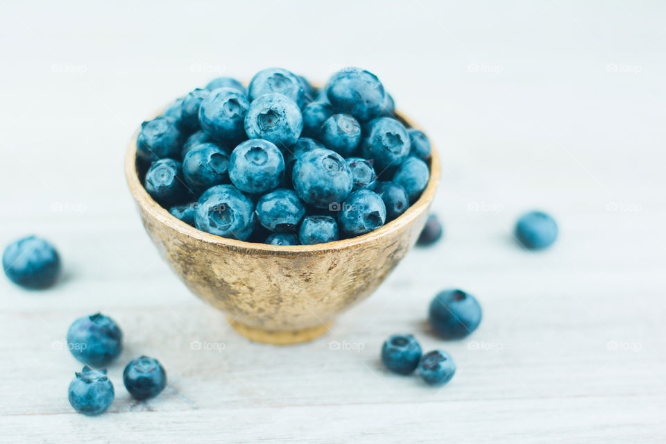 Gold Bowl Full of Fresh Blueberries on a White Tabletop