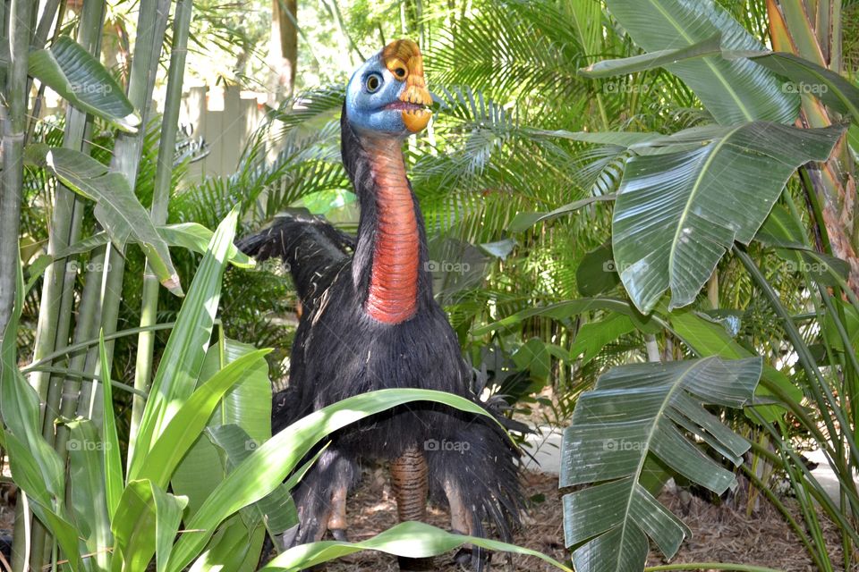 A bird-like dinosaur with a red neck standing amongst the trees