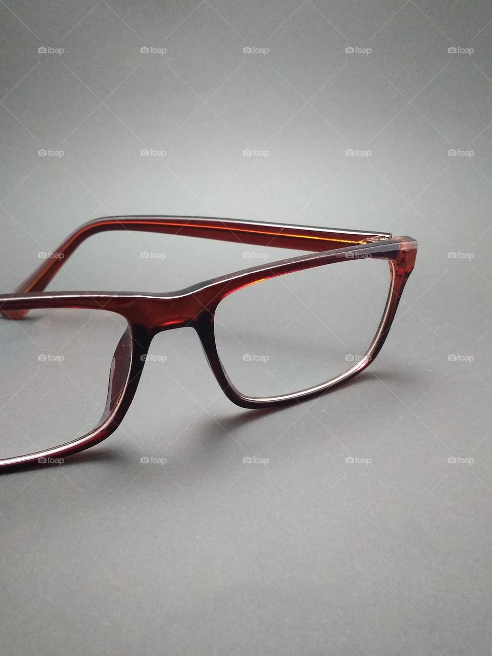 Transparent reading glasses with brown frames photographed in studio close-up on grey background.