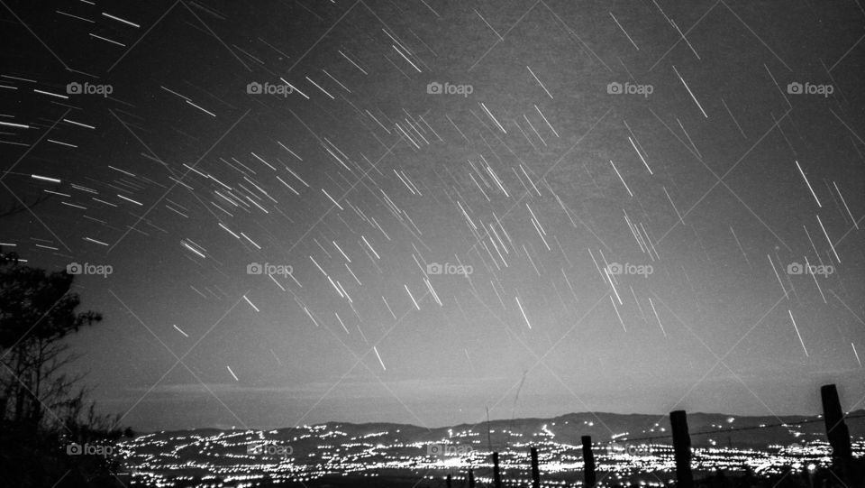 long exposure photo of stars called star trail on top of a mountain overlooking the city lights