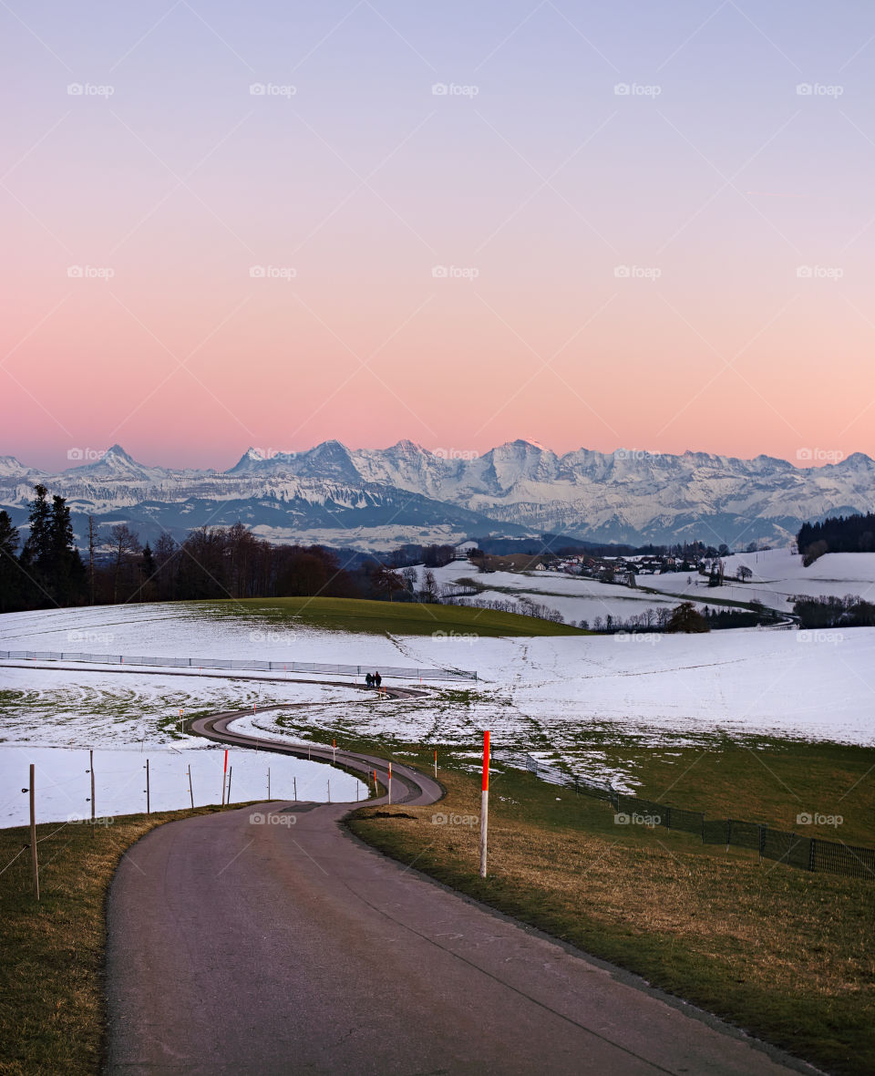 Pathway leading through snow covered hills with alpine mountain range in background