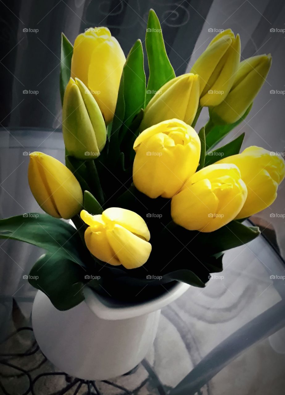 a bunch of yellow tulips flowers in a white jar on a glass table close up top view spring