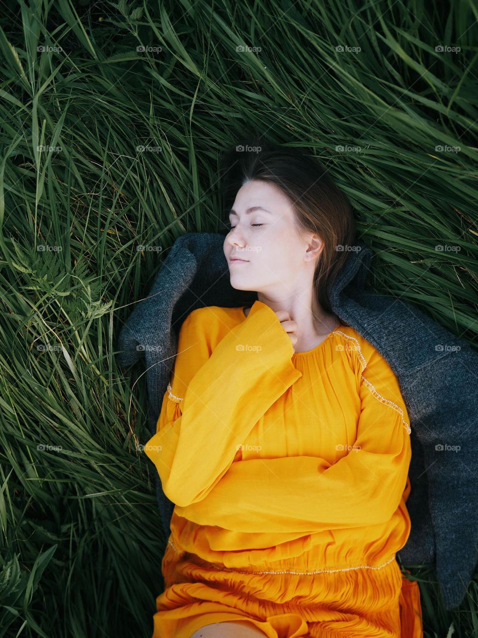 A young beautiful girl in a yellow dress lies on the green grass on a summer day, closed eyes, portrait of woman 