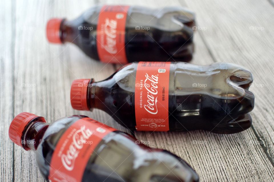 Three plastic bottles of Coca-Cola on a white rustic background