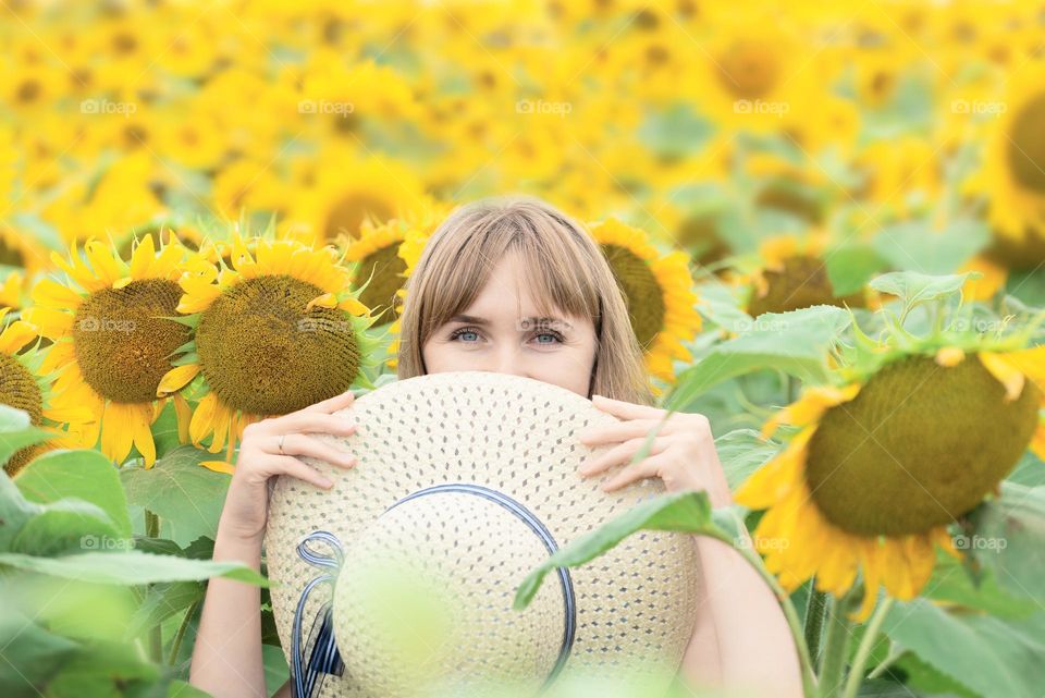 Young woman with a hat in a field of bright yellow sunflowers. Summer concept. Greeting card with selective focus. 