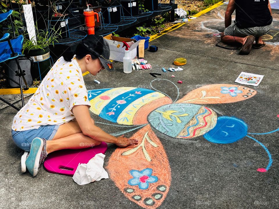 Woman drawing a colorful bee in a sidewalk chalk art competition 
