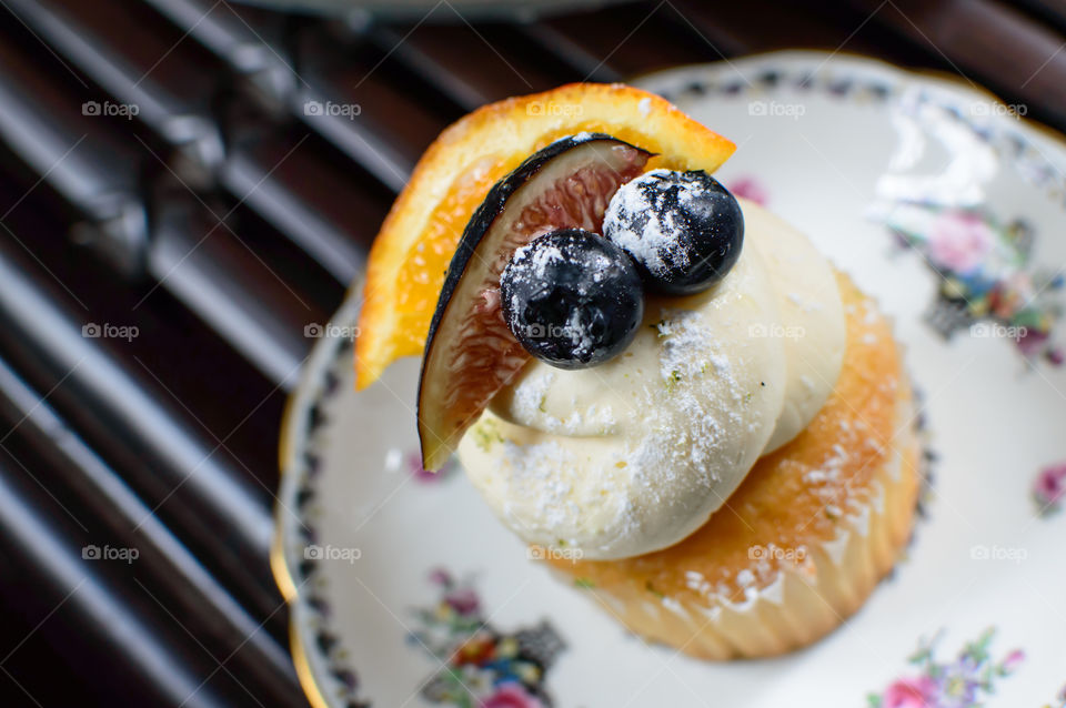 Vanilla Fruit and cream cupcake on plate on rattan table decorated with white frosting slice of orange, fig and fresh blueberry 