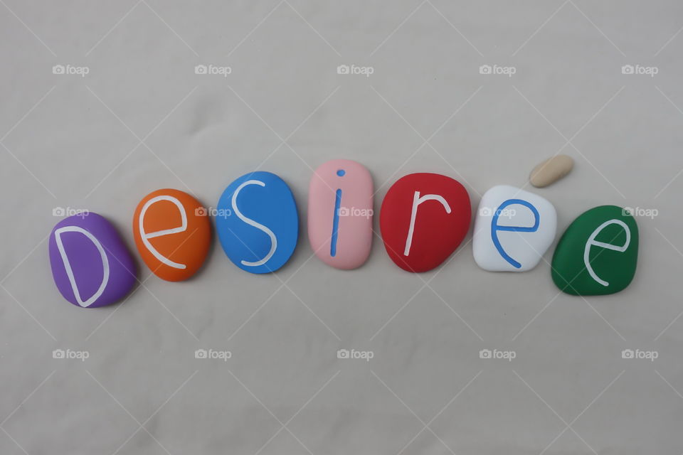 Desirée, feminine given name composed with colored and carved stones over white sand