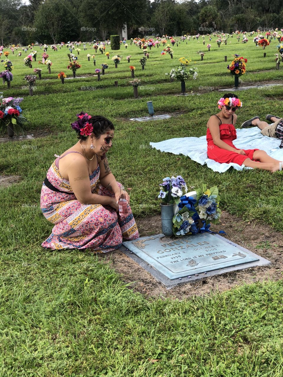 Mother And daughter celebrate Day of the dead  with a picnic to remind their Grandfather that he may be gone but  he is not forgotten, dead flowers are a reminder that we need to visit more often.