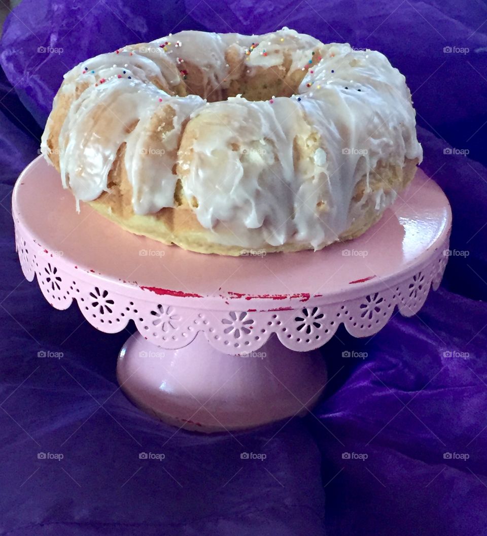 Cake doughnut bundt cake rests on a mostly pink vintage cake stand. 