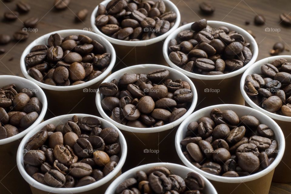 Small paper cups filled with coffee beans arranged in a pattern against a dark wood background 