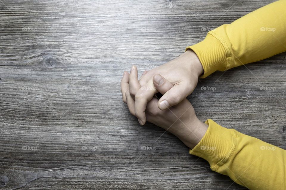 Men's hands in a yellow jacket lie on a gray wooden surface, which is used as a background or a surface with incident light.