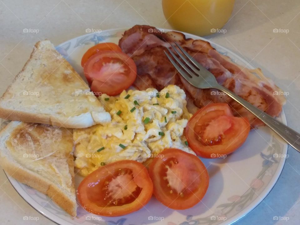 breakfast of bacon scrambled eggs tomatoes toast and juice