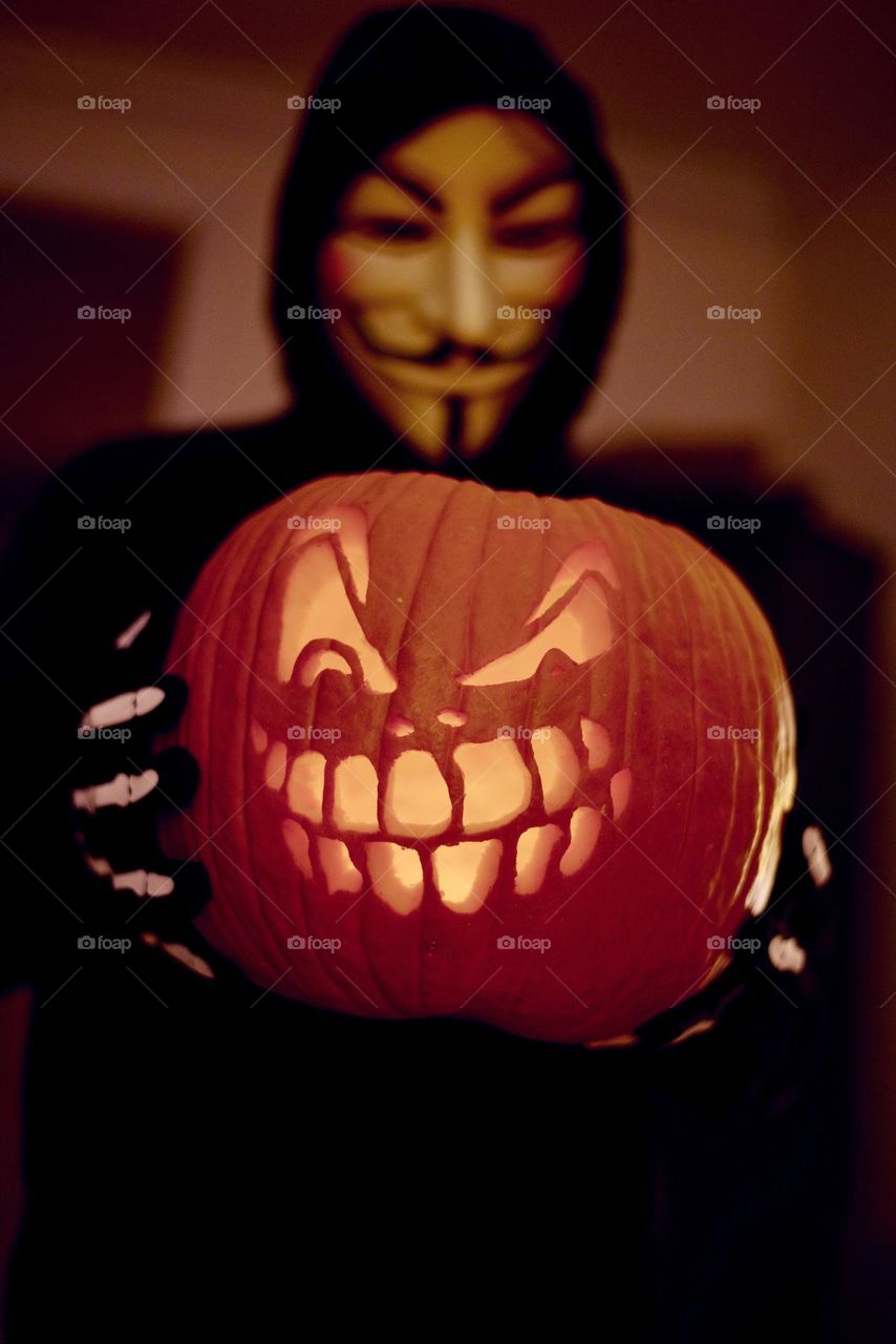 Halloween spirit, Guy Fawkes costume holding carved jack-o’-lantern