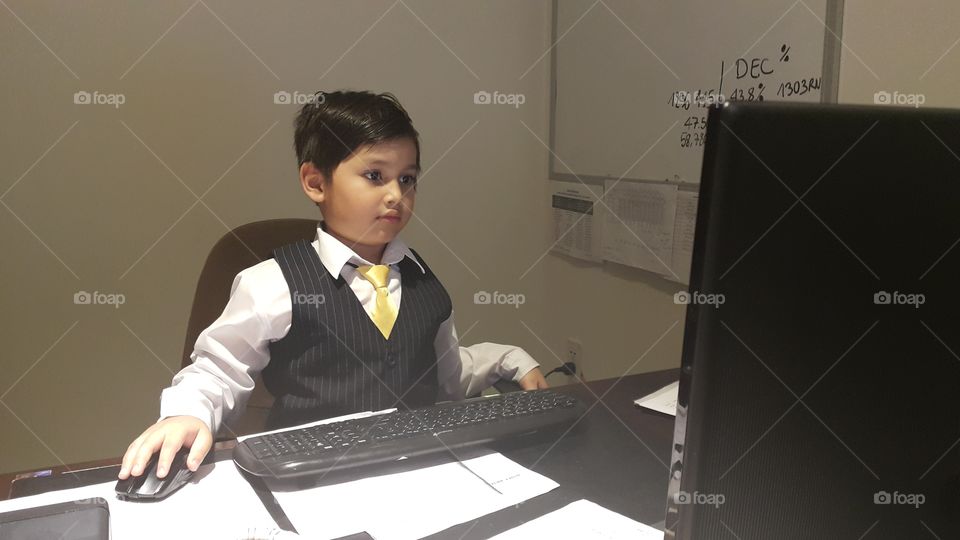 Young boy dressed as business man sitting in office working on a computer