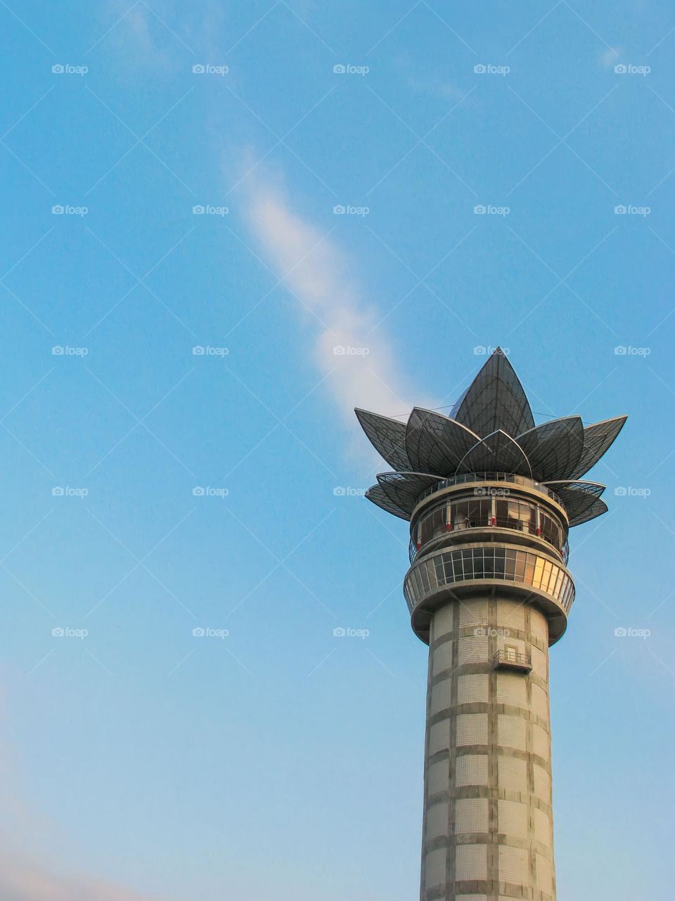 a tower with an open flower structure at the top, against a backdrop of a blue sky with wispy clouds