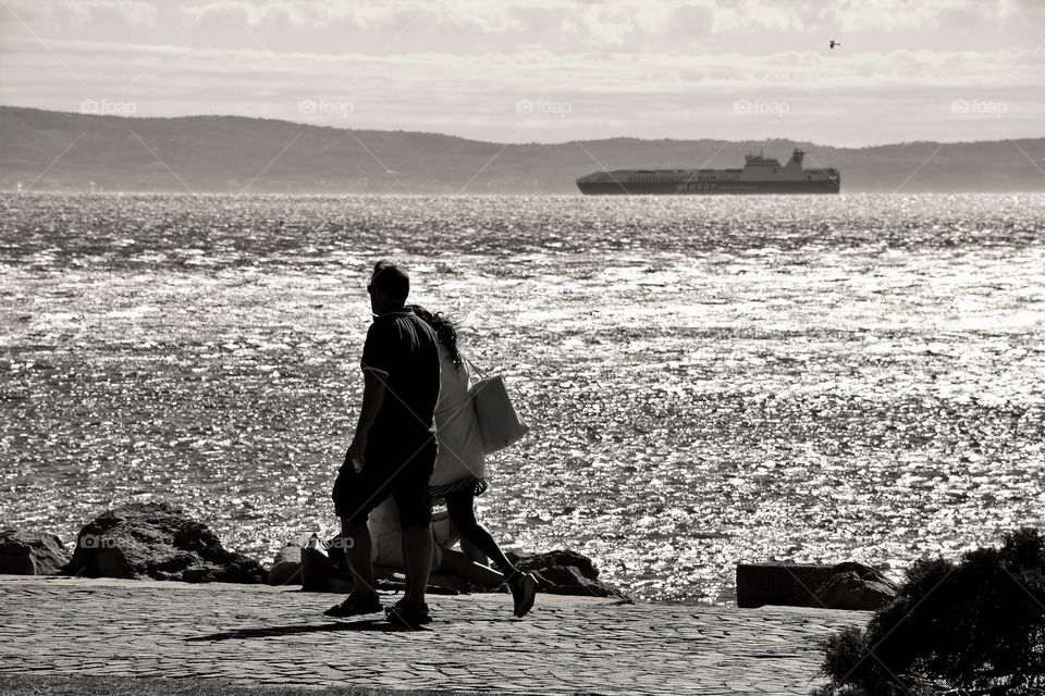 Couple walking down the seashore with horizon over water, Italy
