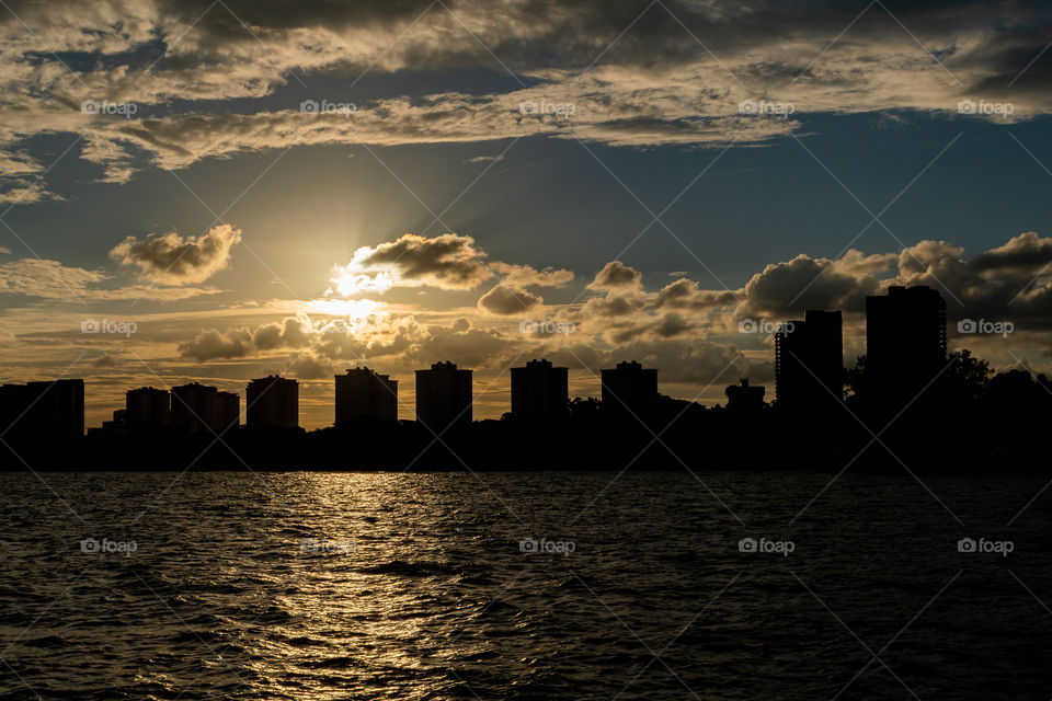 Sunset by the bay with cloudy blue sky and silhouette of buildings in the background
