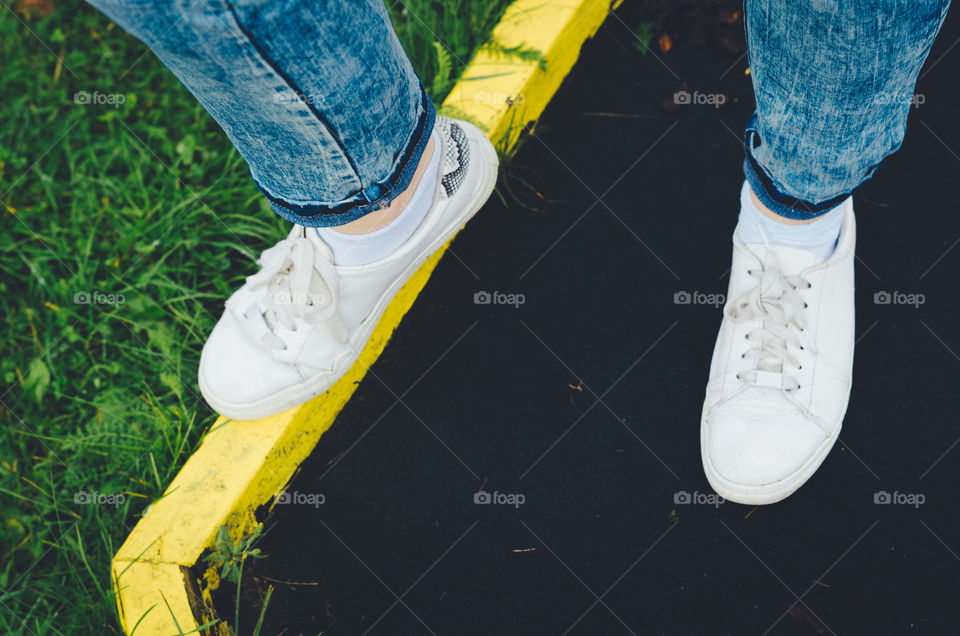 Top view of girl's legs in bright white sneaker shoes and blue jeans standing on a golf course.