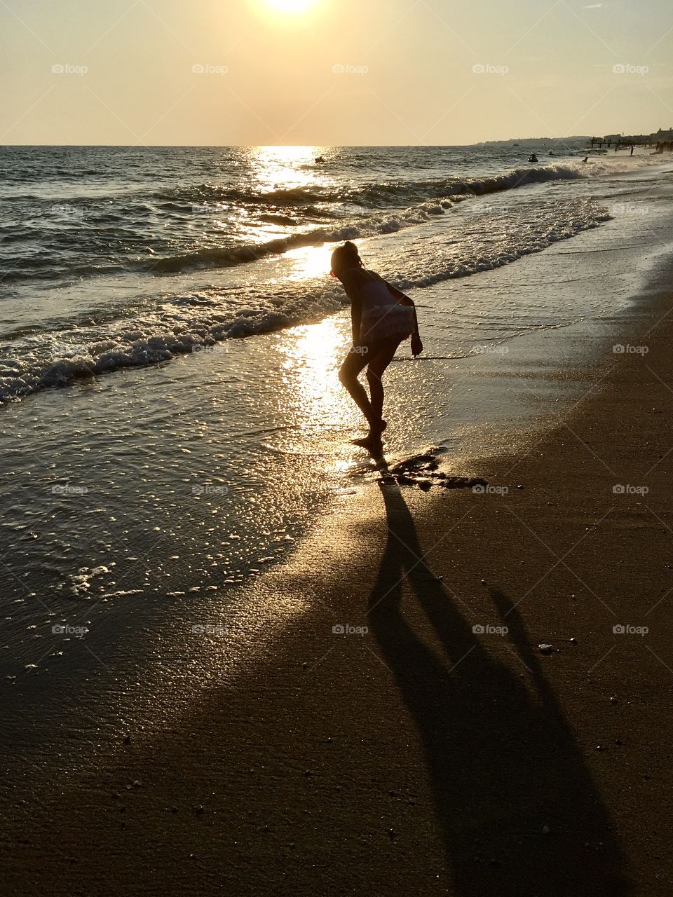 little girl looking for shells and pebbles during sunset on the beach