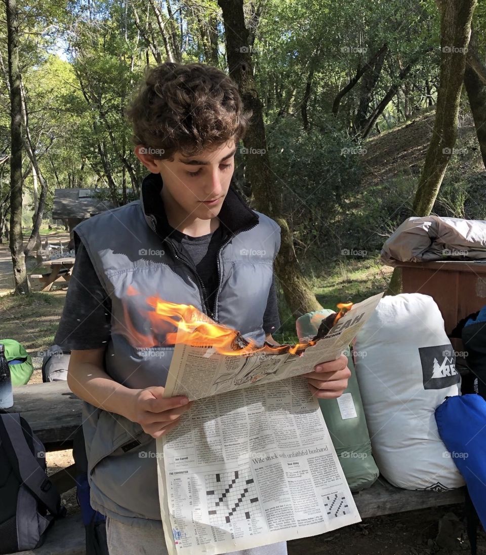 Reading newspaper on fire camping in forest 